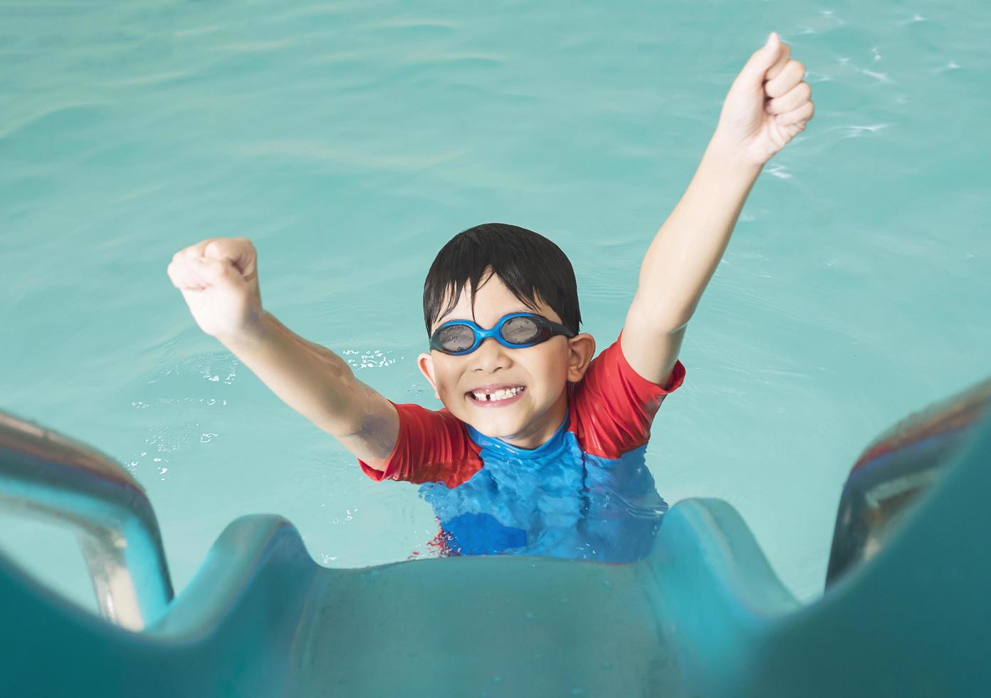 bambino felice asiatico che gioca a cursore in piscina foto