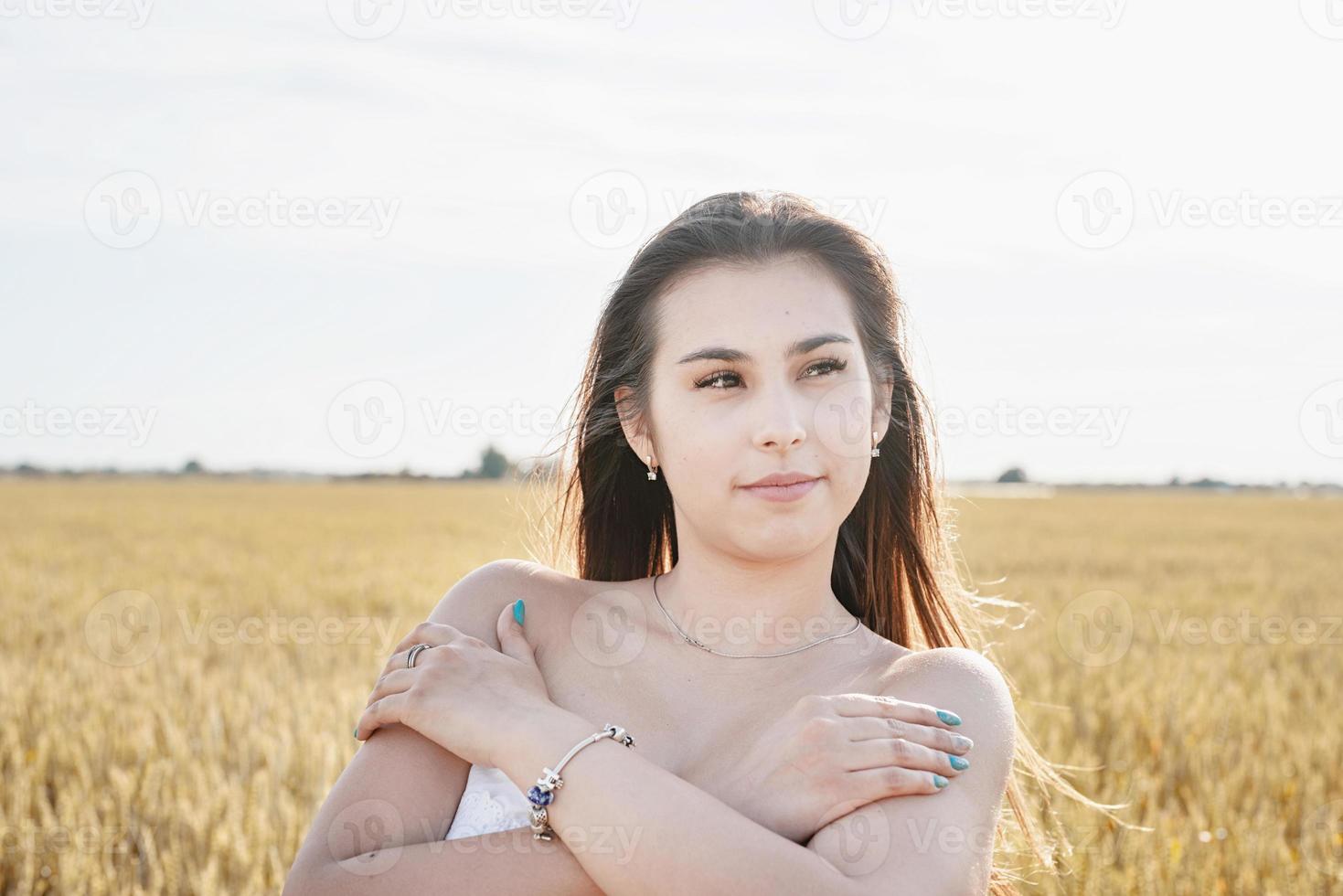 giovane donna in abito bianco in piedi su un campo di grano con l'alba sullo sfondo foto