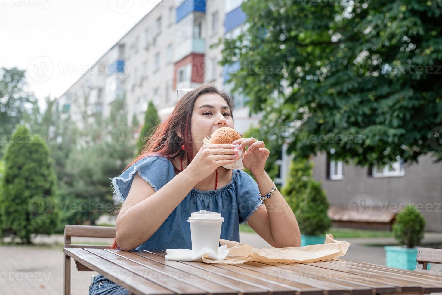 elegante donna millenaria che mangia hamburger al caffè di strada in estate foto