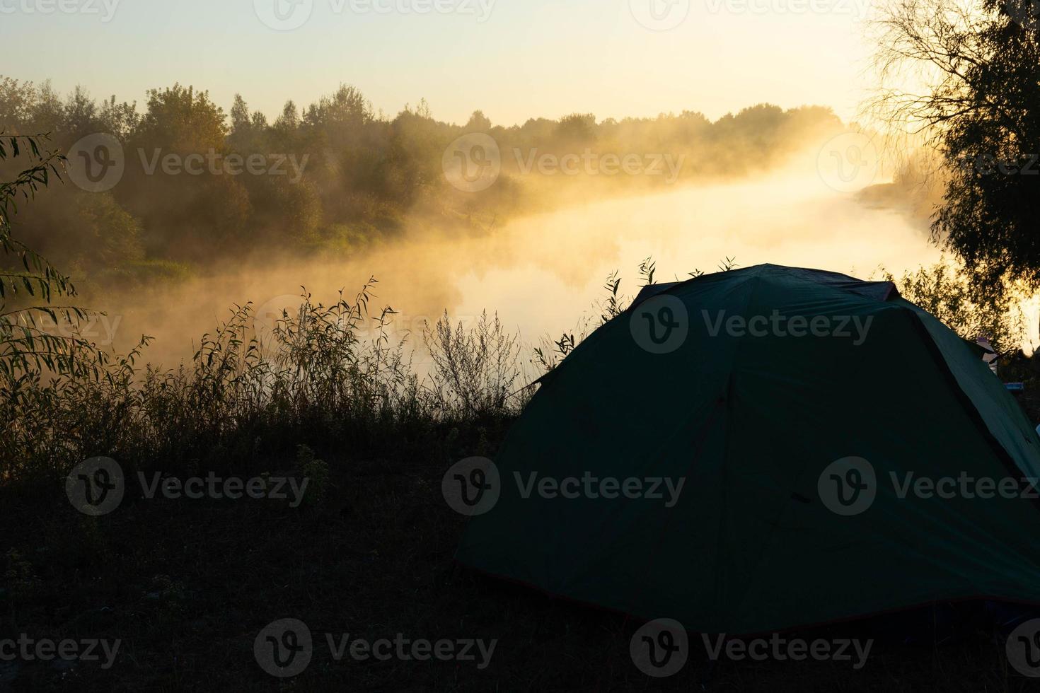 tenda turistica verde vicino al fiume all'alba, con nebbia mattutina autunnale sull'acqua. paesaggio turistico all'aperto. foto