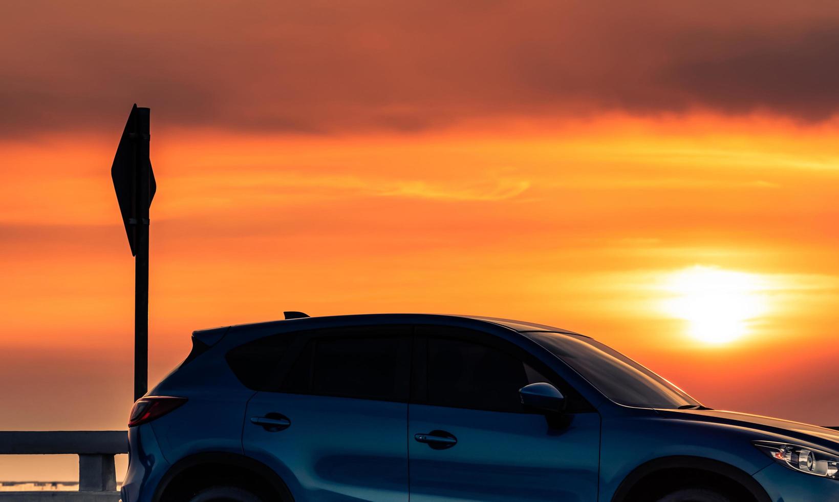 vista laterale di un'auto suv blu con design sportivo e moderno parcheggiata su strada di cemento al tramonto. tecnologia per auto ibride ed elettriche. viaggio su strada. industria automobilistica. auto di lusso con bellissimo cielo al tramonto. foto