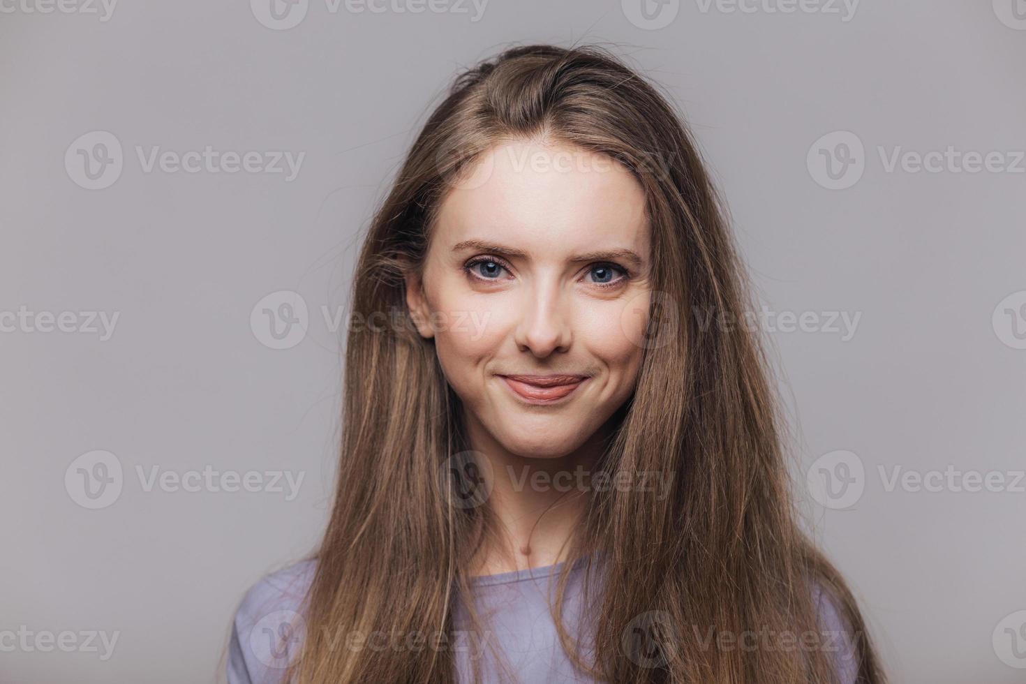 bruna deliziato modello femminile dagli occhi azzurri con espressione soddisfatta, felice di ricevere complimenti, isolato su sfondo grigio. bella giovane donna dai capelli scuri si sente contenta, modella in studio foto