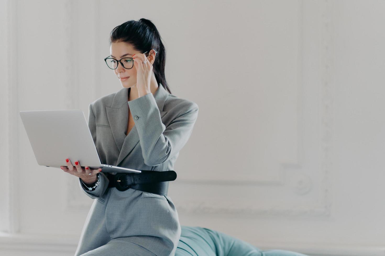 elegante banchiere professionista concentrato sullo schermo del computer portatile, vestito con abiti formali, legge documenti in versione online pone in una stanza spaziosa, ufficio a casa. affari, concetto di tecnologia foto