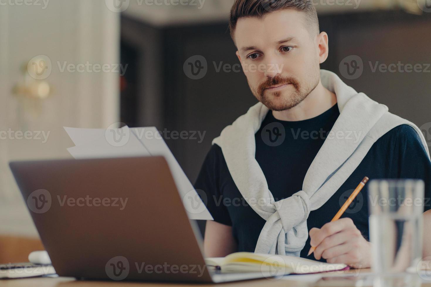 uomo d'affari impegnato che usa il laptop e prende appunti sul suo posto di lavoro foto