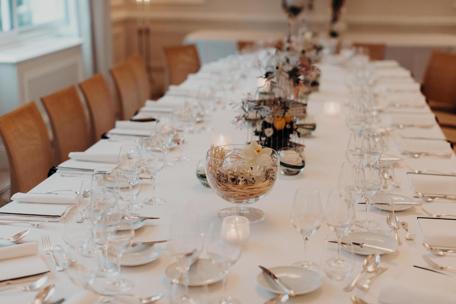 sala banchetti del ristorante con tavolo da pranzo splendidamente decorato con bicchieri e piatti senza persone intorno. occasione speciale e concetto di celebrazione foto