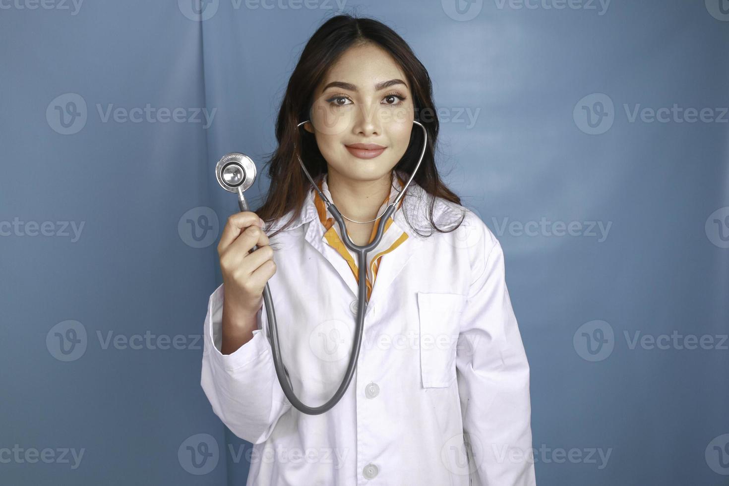 ritratto di una giovane donna asiatica medico, un medico è sorridente e indossa uno stetoscopio isolato su sfondo blu foto