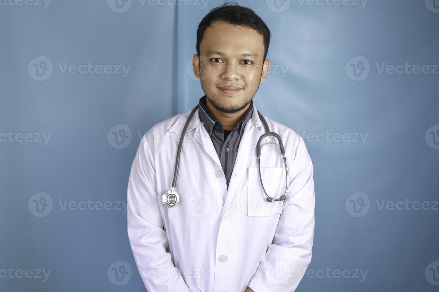 ritratto di un medico maschio attraente fiducioso, braccia sorridenti amichevoli incrociate indossare uno stetoscopio bianco da laboratorio isolato colore blu di sfondo foto