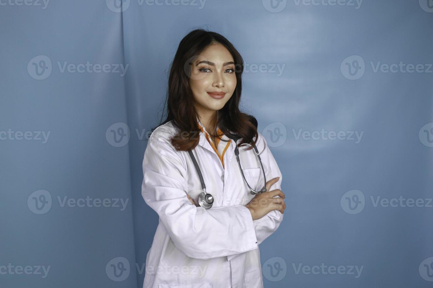 ritratto di una dottoressa attraente e sicura, braccia sorridenti amichevoli incrociate indossare uno stetoscopio bianco da laboratorio isolato colore blu di sfondo foto