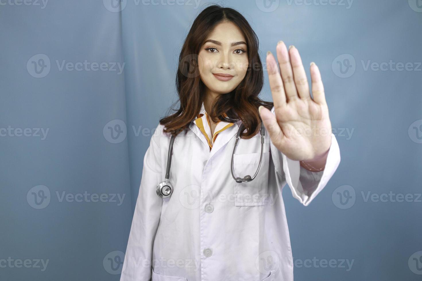 medico femminile asiatico serio con lo stetoscopio e il camice bianco, mostrando il segnale di stop. foto