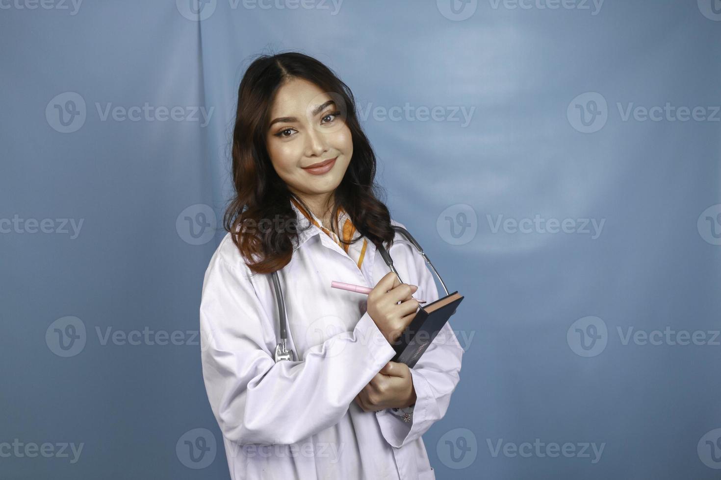 ritratto di una giovane donna asiatica medico, un medico è sorridente e in possesso di note isolate su sfondo blu foto