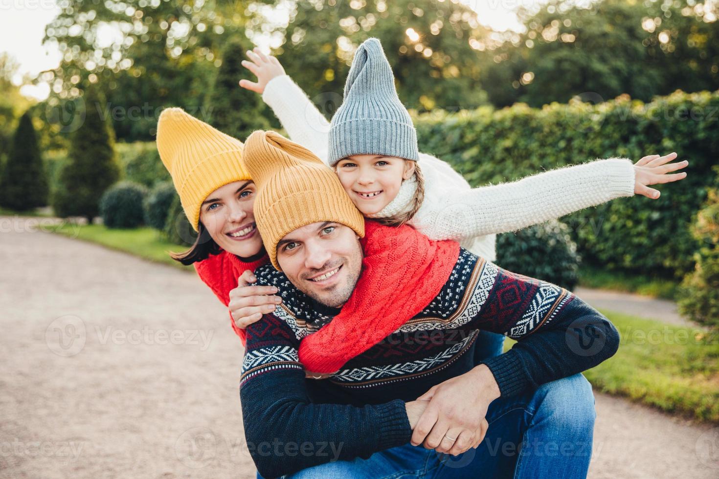 divertirsi insieme sorridente donna eccitata, uomo e la loro bambina, indossare abiti caldi a maglia, abbracciarsi, camminare nel parco, essere di buon umore. la famiglia dà sostegno, incoraggiamento foto