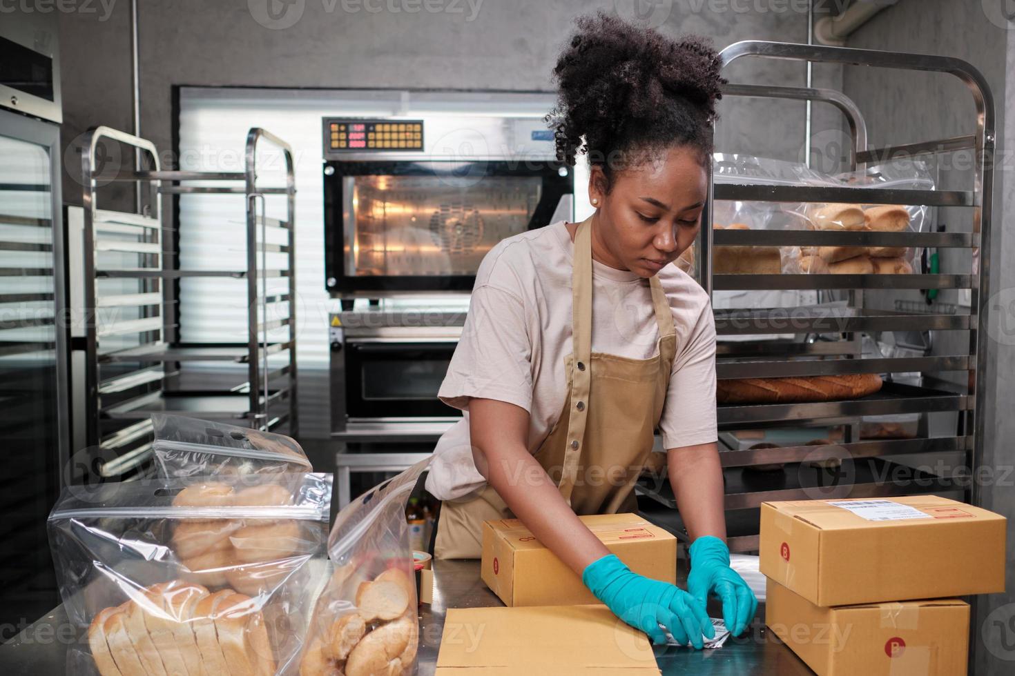 consegna di piccole imprese di avvio di prodotti da forno. una cuoca afroamericana sta imballando pane e dolci fatti a mano e appena sfornati in scatole e inviando per gli acquisti dei clienti online nella cucina culinaria. foto