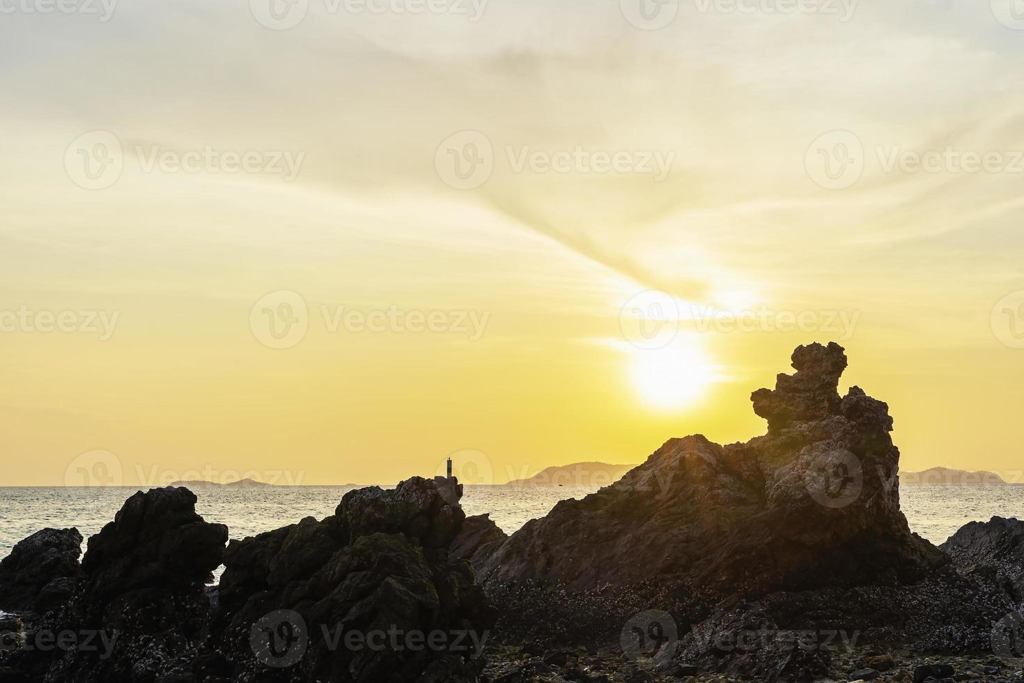 primo piano della roccia in primo piano di fronte al mare al crepuscolo. silhouette roccia sulla spiaggia contro il cielo durante il tramonto. sole che tramonta all'orizzonte per la libertà e l'inizio del concetto di vita. foto