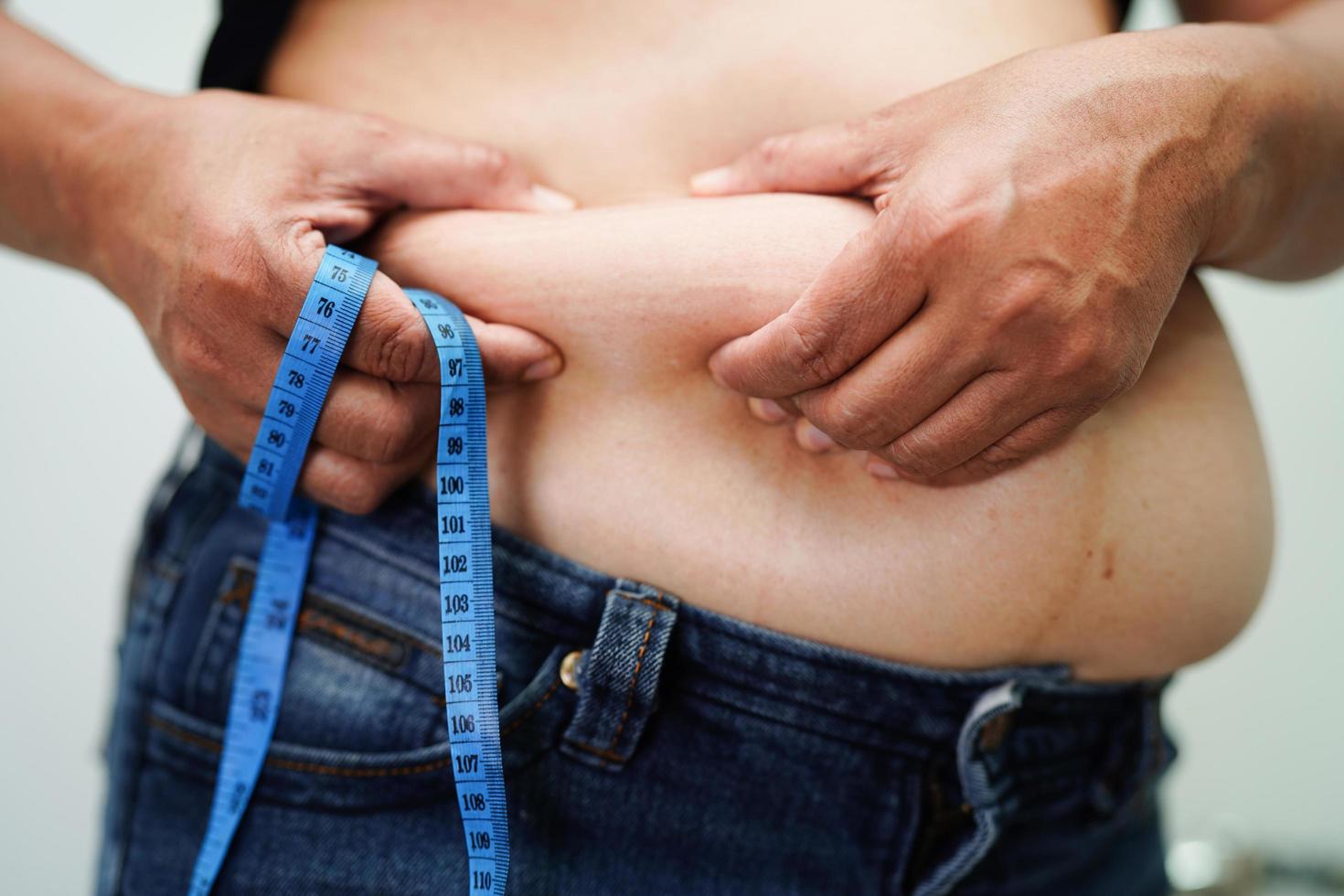 donna asiatica in sovrappeso usa la mano per spremere la pancia grassa di grandi dimensioni sovrappeso e obesità. foto