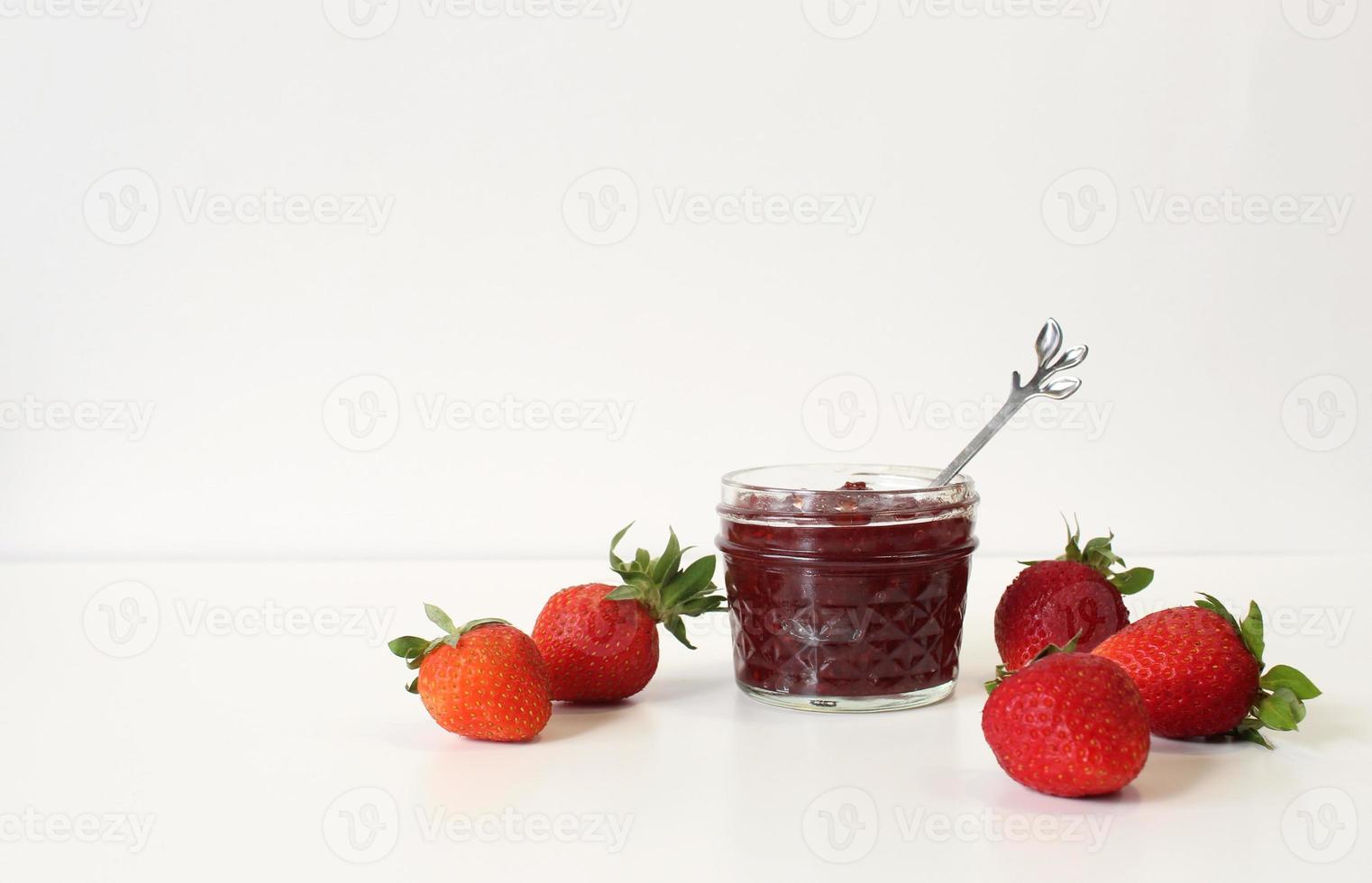 conserve di fragole fatte in casa o confetture in barattolo di vetro circondate da fragole fresche biologiche. messa a fuoco selettiva con sfondo bianco. foto