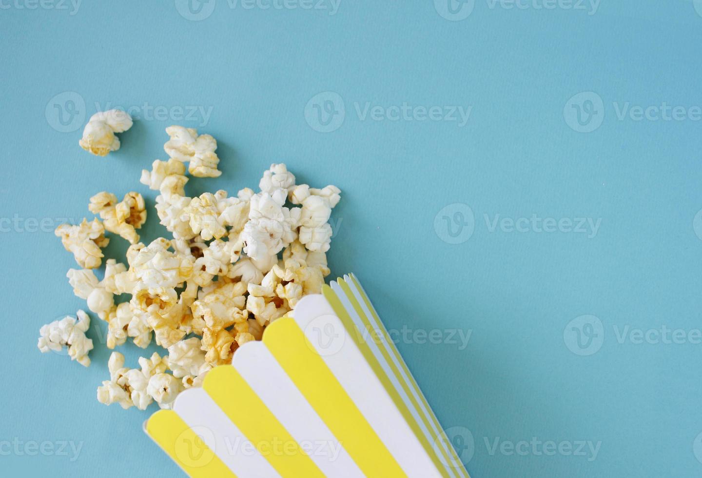 popcorn rovesciato e secchio di carta su sfondo blu. concetto di notte di film. copia spazio per il testo foto