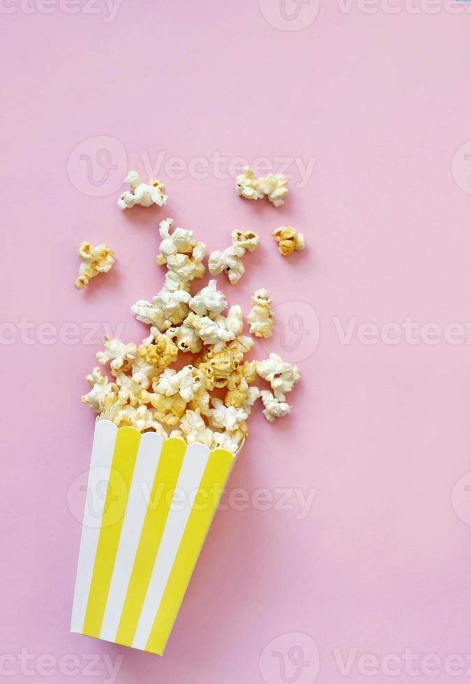 popcorn rovesciato su sfondo rosa. concetto di notte di film. copia spazio per il testo foto