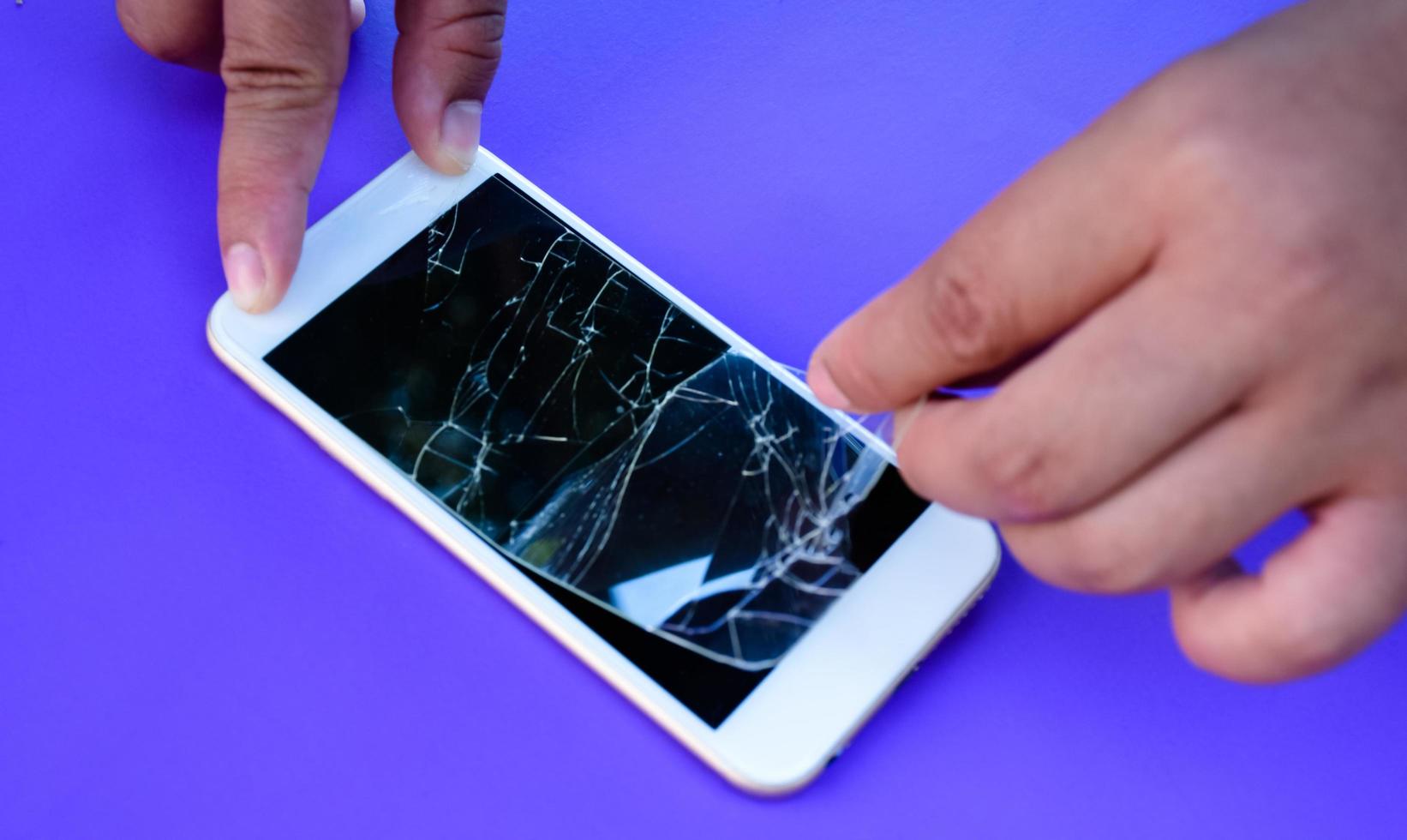 il riparatore sta estraendo la pellicola di plastica trasparente rotta dal telefono cellulare touch screen per cambiare quella nuova. messa a fuoco morbida e selettiva. foto