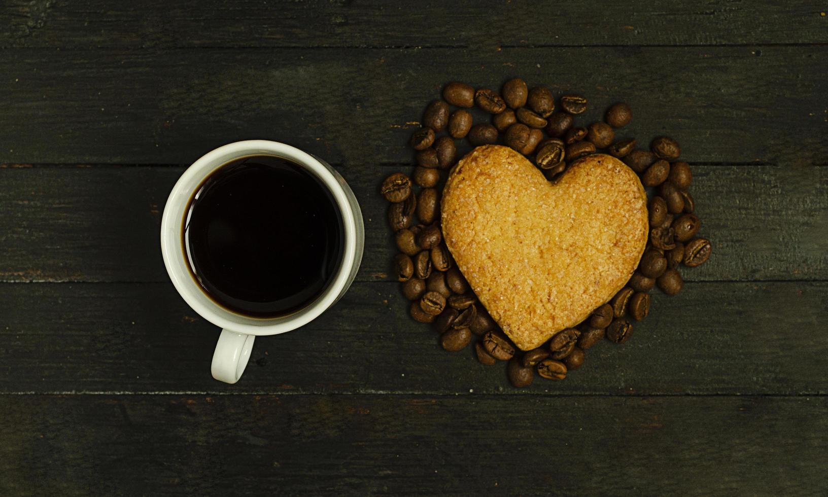 una tazza di caffè e un biscotto d'amore con chicchi di caffè su una superficie di legno, vista dall'alto. Vacanze di San Valentino. foto