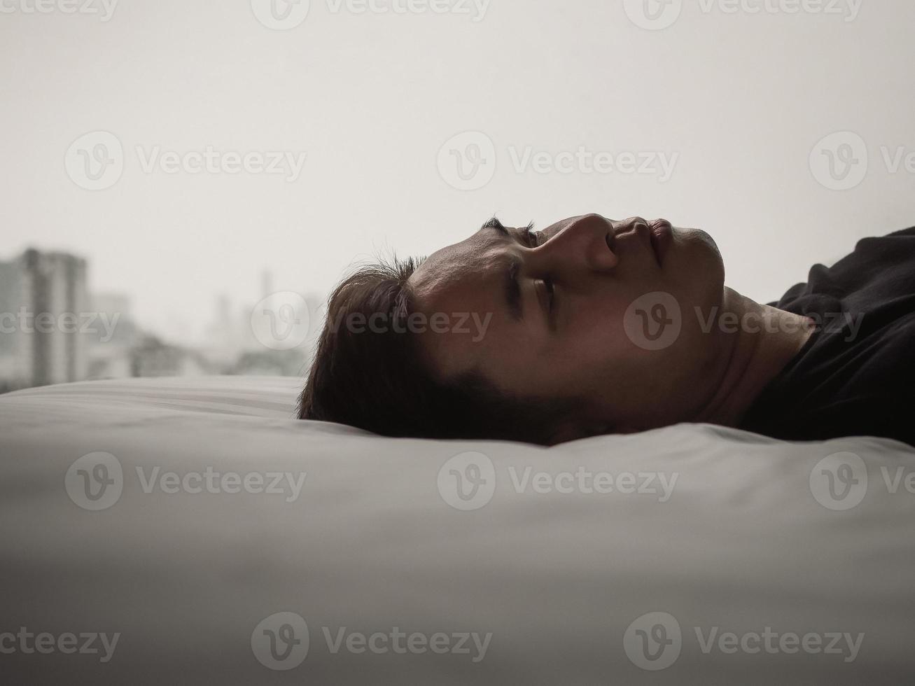 l'uomo asiatico si sente triste da solo sul letto con lo sfondo della città. resta a casa, concetto di depressione e solitudine. foto