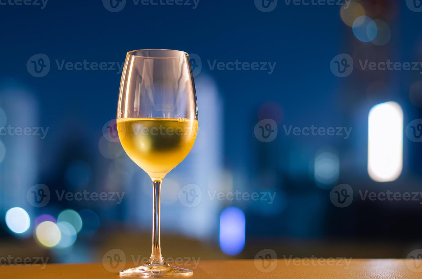 un bicchiere di vino bianco mette sul tavolo sul balcone con sfondo sfocato della città. concetto di relax a casa. foto