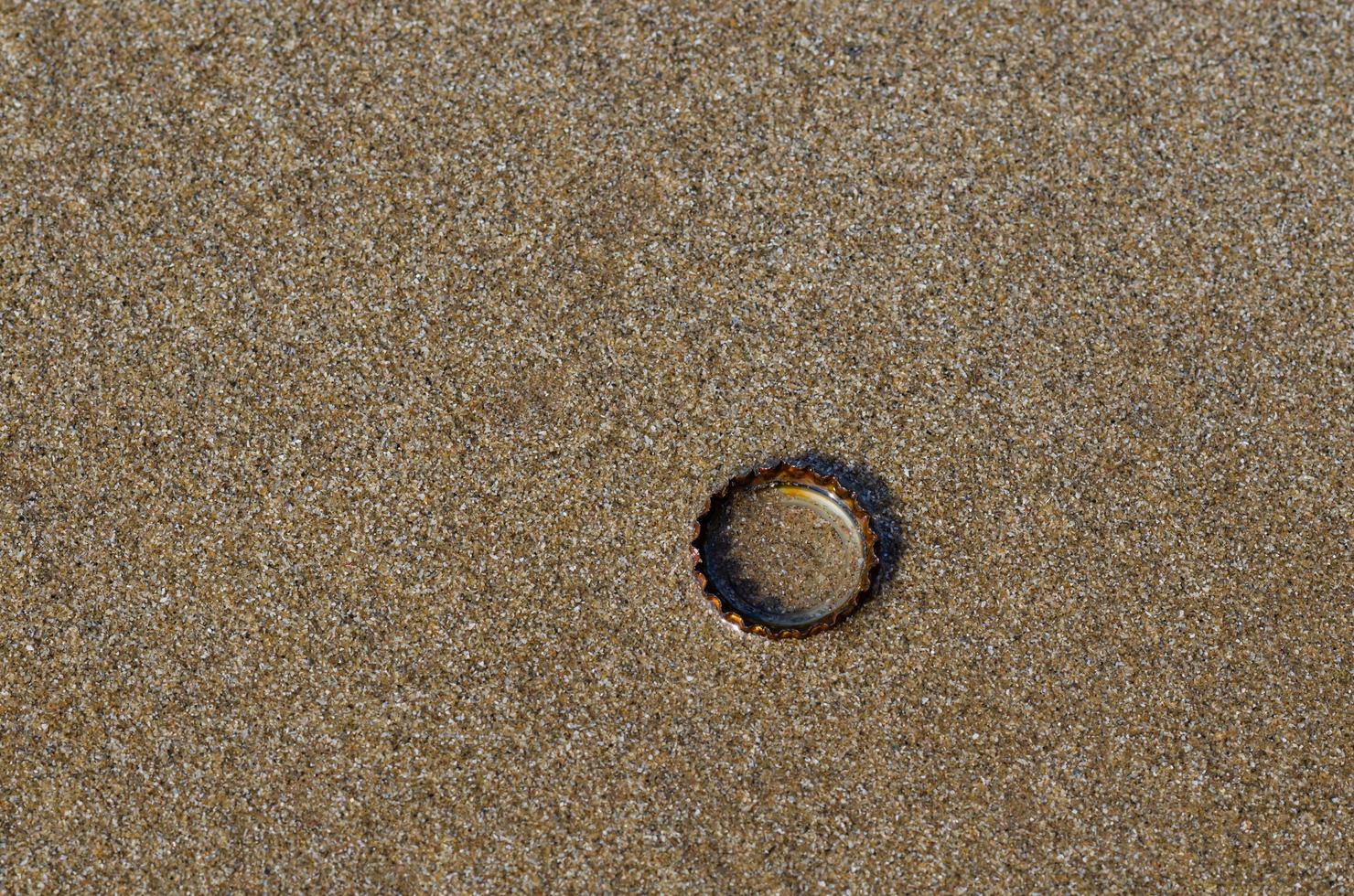 un tappo di bibita con ruggine sulla sabbia bagnata e pulita della spiaggia con ombra dalla luce solare. foto