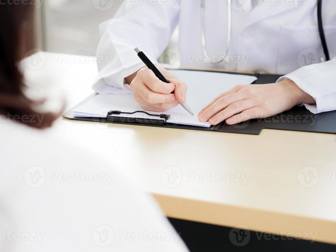 un primo piano della mano di una dottoressa o di un'infermiera sta usando una penna per scrivere informazioni o qualcosa con una paziente sfocata in primo piano. foto