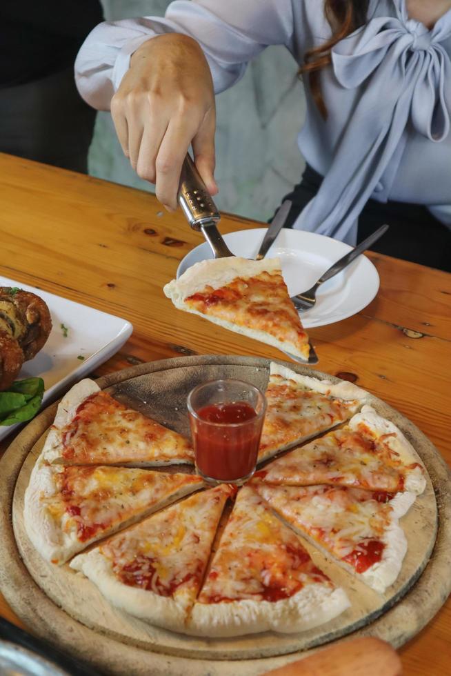 una giovane donna è felice di vedere il cibo in tavola e scegliere il menù della pizza da mangiare con buon gusto. i menù pizza sono perfetti per i banchetti tra amici e familiari in quanto sono comodi da mangiare foto