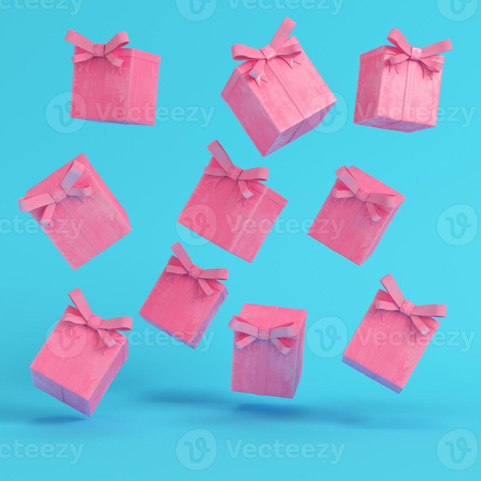 scatole regalo volanti rosa con fiocco a nastro e palla di Natale su sfondo blu brillante in colori pastello foto