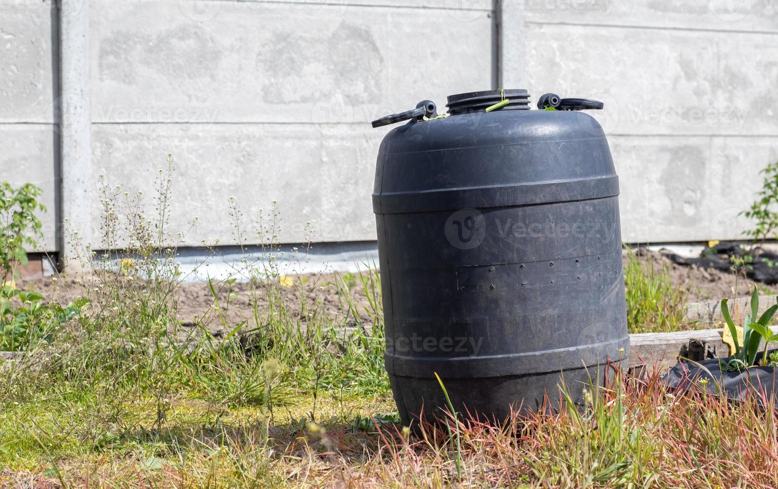 grande fusto di plastica nera con acqua nel giardino estivo. serbatoio dell'acqua piovana in giardino, calda giornata estiva. botti per innaffiare il giardino. foto