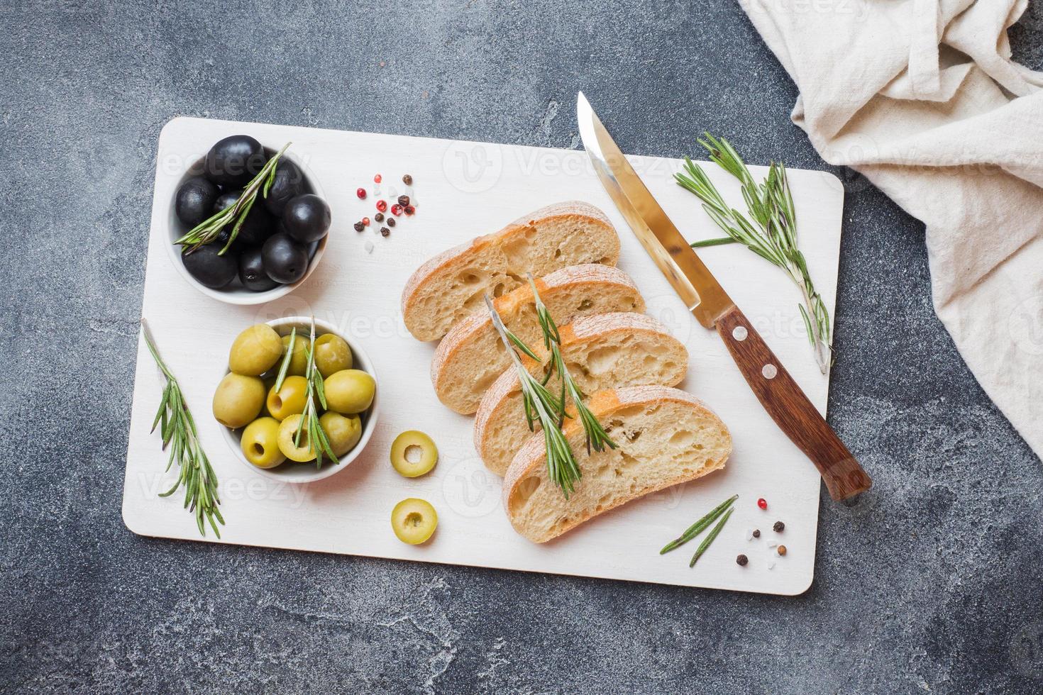 ciabatta italiana con olive e rosmarino su un tagliere. sfondo di cemento scuro. copia spazio. foto