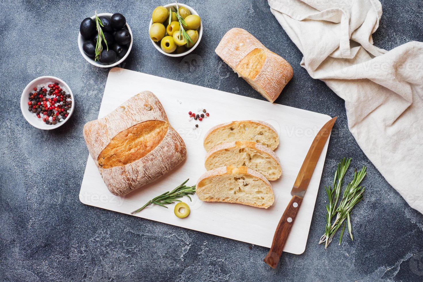 ciabatta italiana con olive e rosmarino su un tagliere. sfondo di cemento scuro. foto