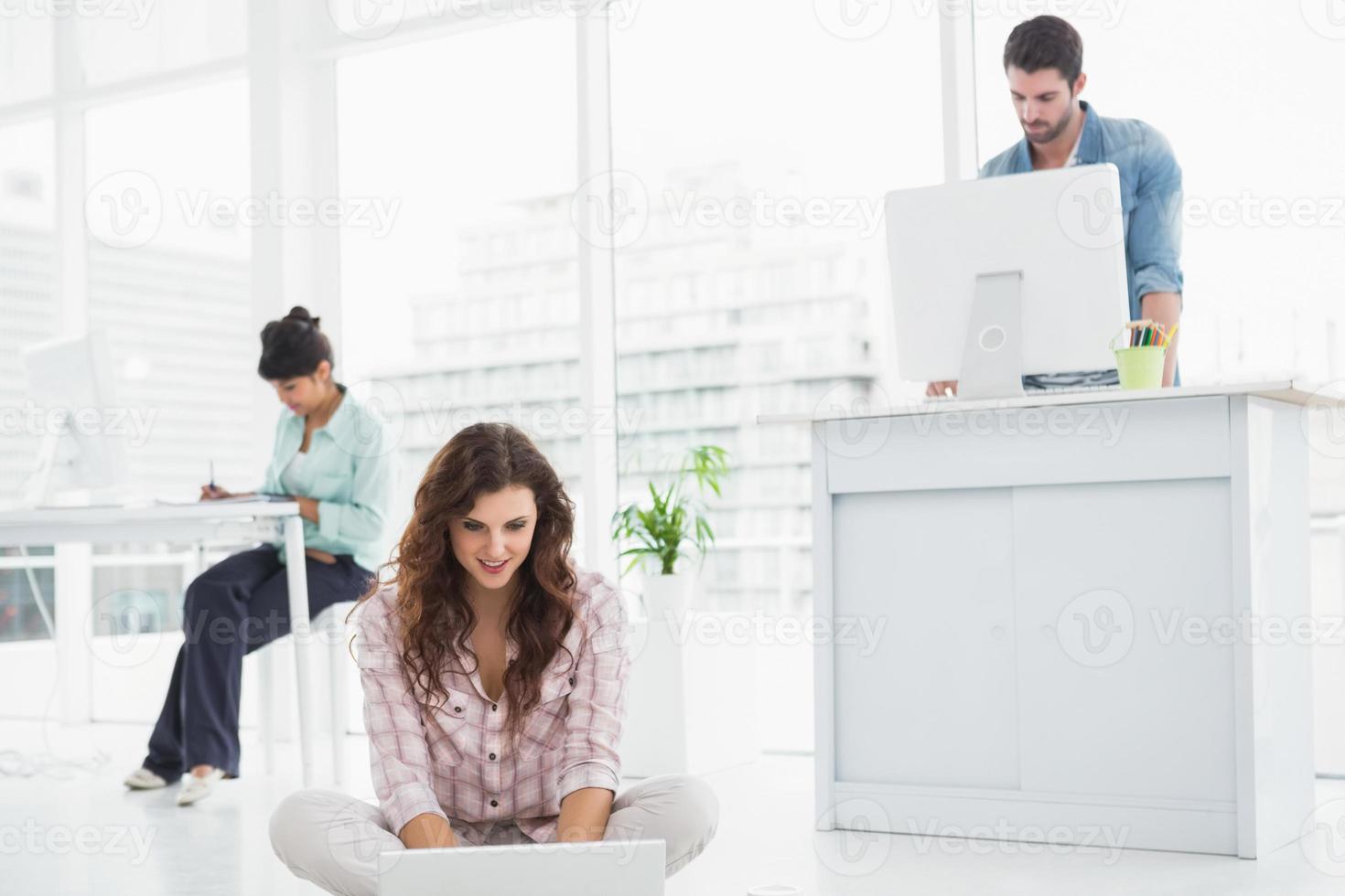 donna di affari allegra che si siede sul pavimento per mezzo del computer portatile foto