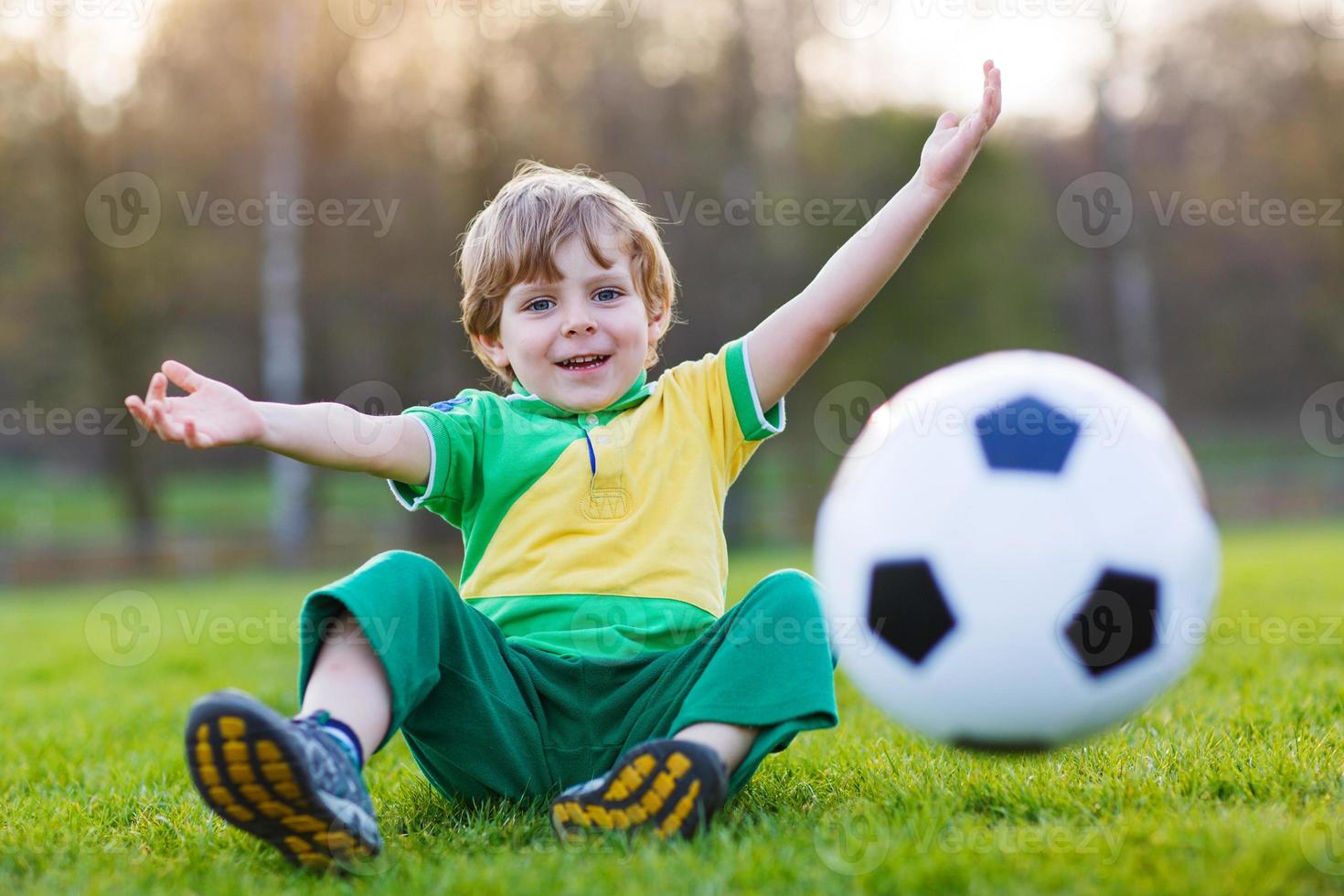 un ragazzo biondo di 4 che gioca a calcio con il campo di calcio onl foto