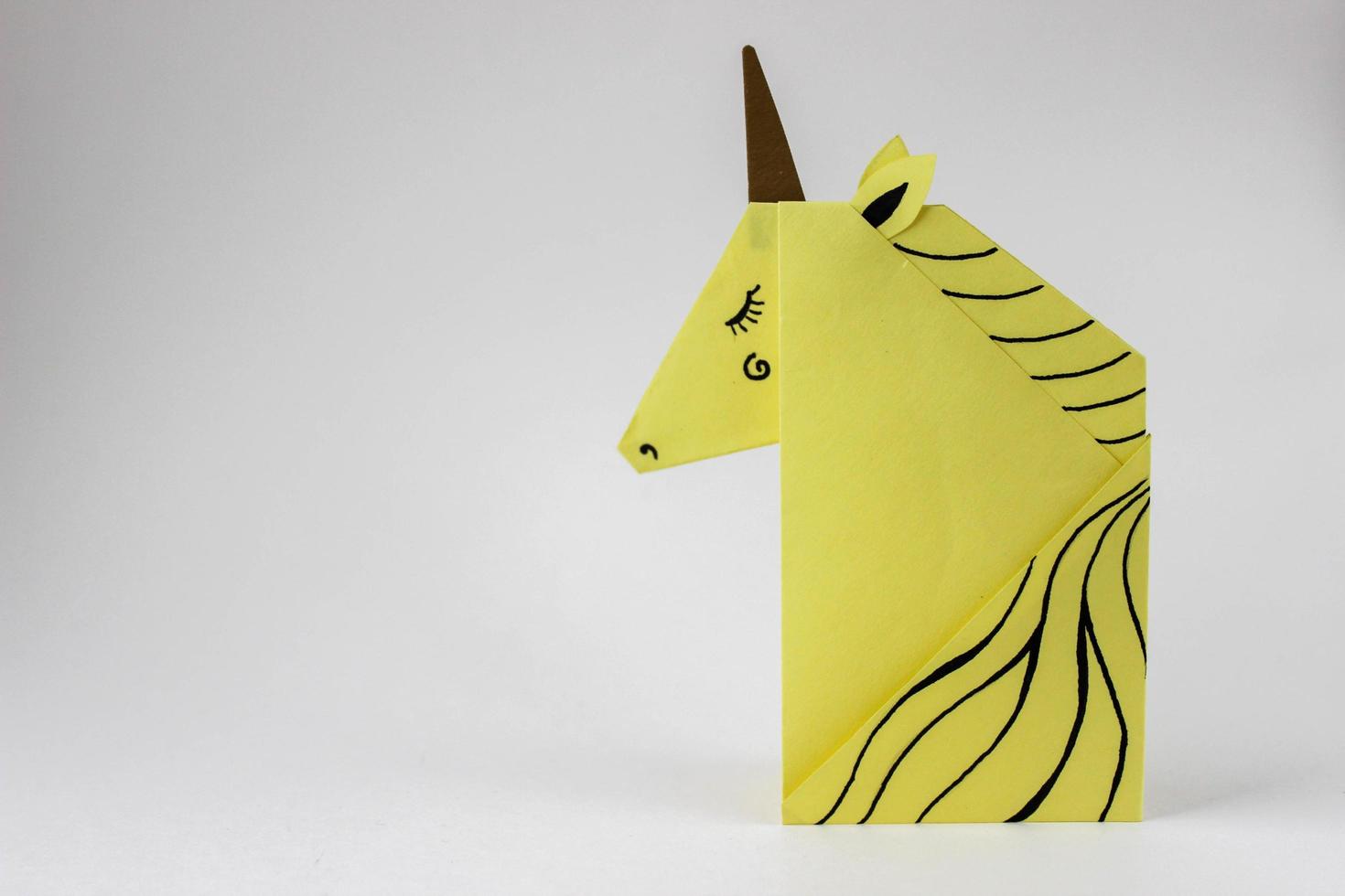 unicorno giallo realizzato con la tecnica dell'origami sul lato destro della foto su sfondo bianco. con posto per il tuo testo.
