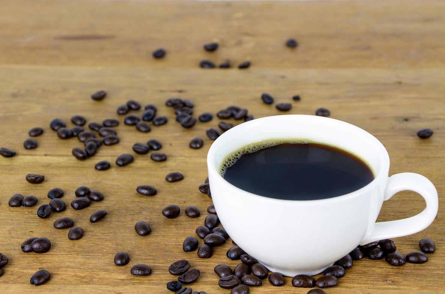 immagine di una tazza in ceramica bianca di caffè americano caldo su un tavolo di legno con chicco di caffè tostato marrone scuro biologico foto