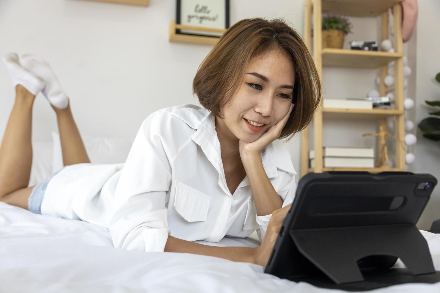 giovane bella ragazza che lavora da casa sul suo letto utilizzando la tavoletta digitale per accedere al suo lavoro di lavoro per lo studio dell'istruzione e il concetto di incontri online foto