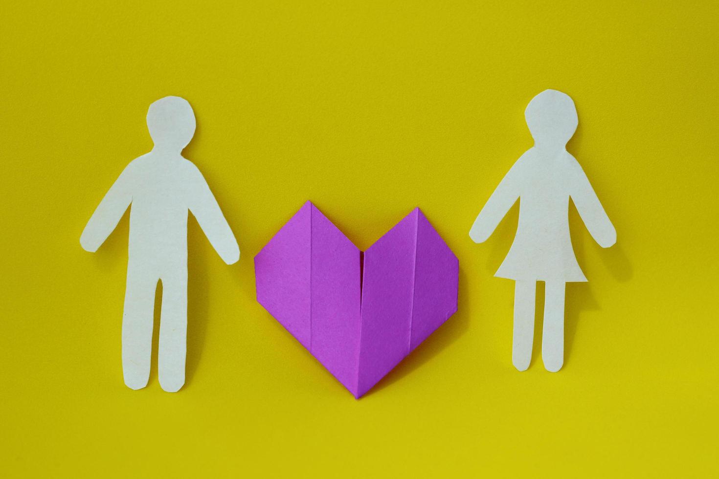 due sagome di uomo e donna sono scolpite su carta bianca con un cuore di origami viola tra di loro su uno sfondo giallo. il concetto di amore, relazioni, famiglia foto
