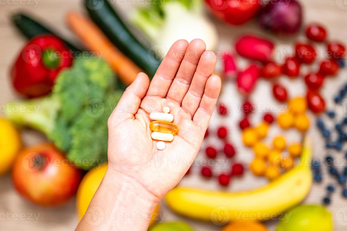 mano che tiene integratori alimentari su frutta e verdura per uno stile di vita sano foto