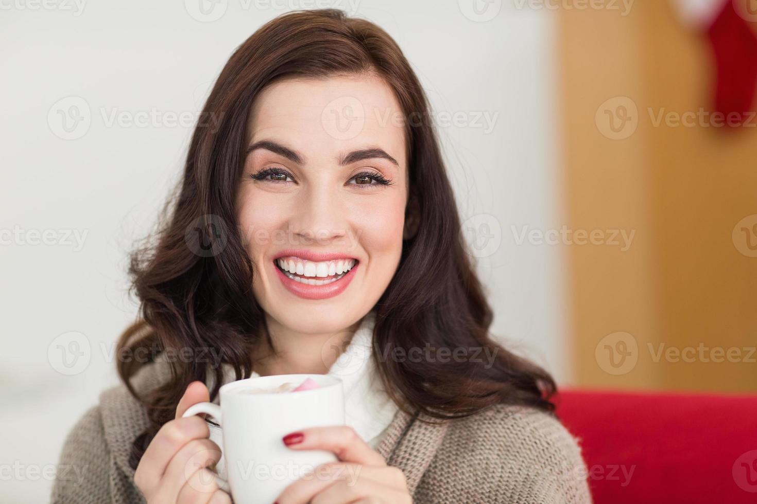 brunette sorridente che gode di una cioccolata calda con la caramella gommosa e molle foto