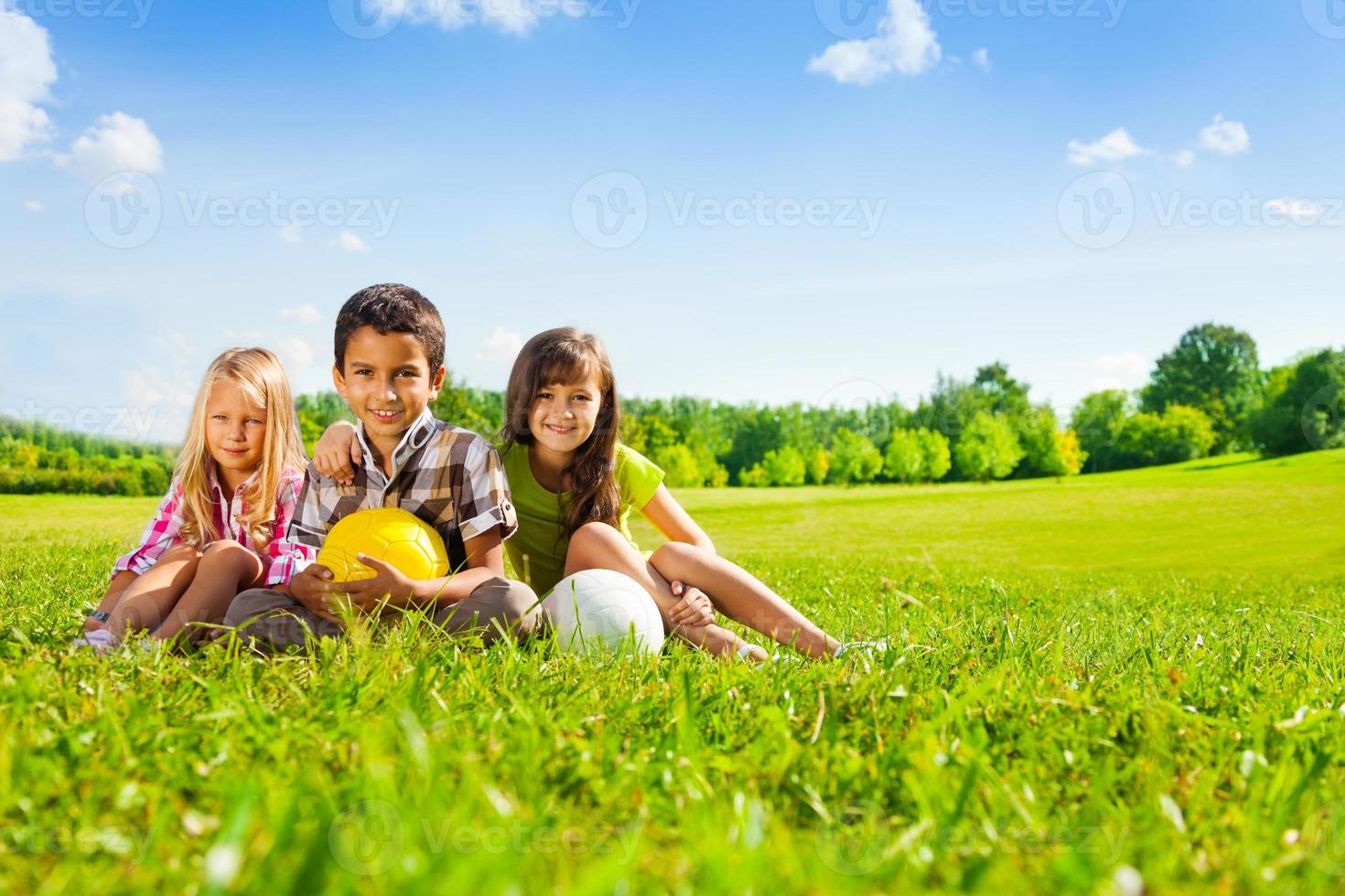 i bambini si siedono sull'erba con le palle dello sport foto