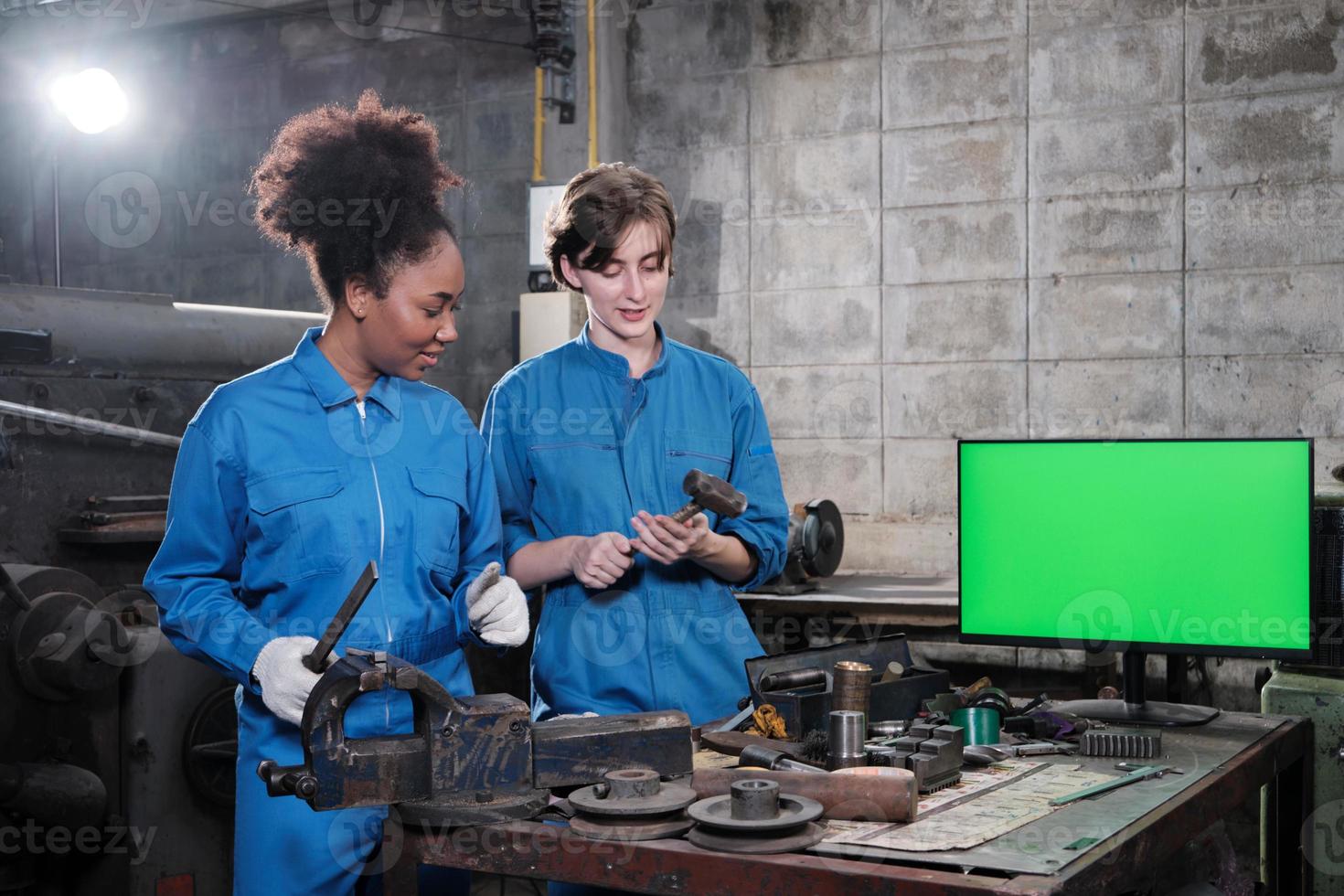 due lavoratrici del settore professionale collaborano in uniformi di sicurezza lavori di carpenteria metallica discutono vicino a monitor con schermo verde, torni meccanici e officina di ingegneria nella fabbrica di produzione. foto