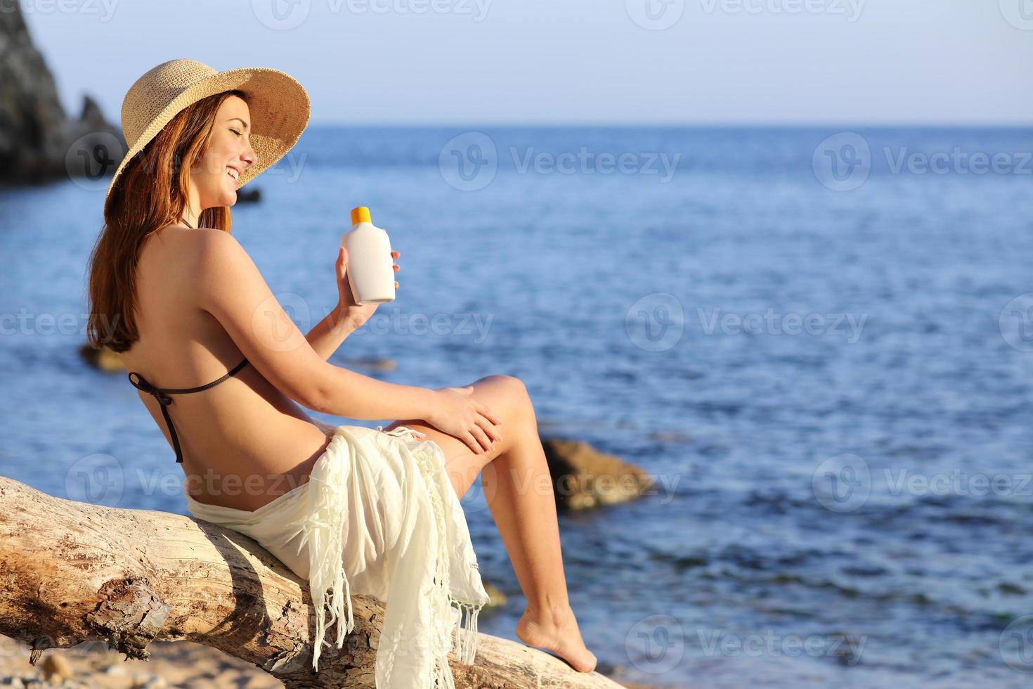 donna in vacanza sulla spiaggia applicando la protezione solare foto