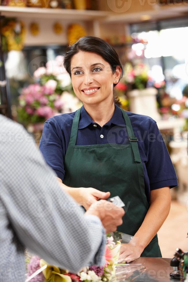 donna sorridente del brunette che viene pagata in un negozio di fiori foto