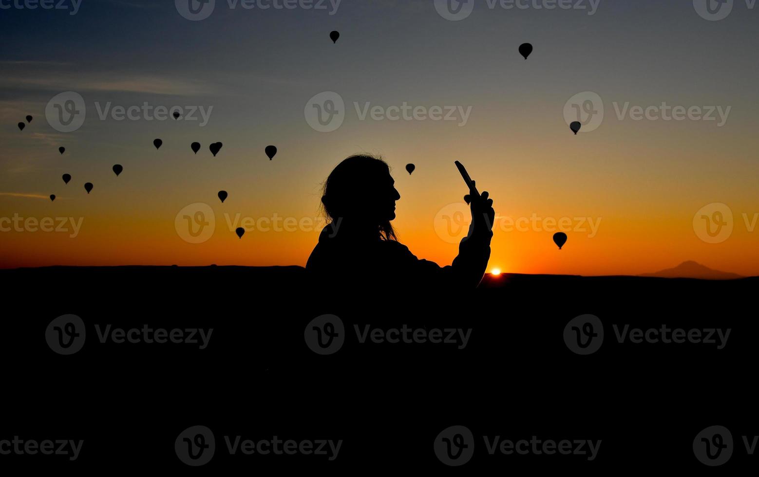 silhouette di smart phone nelle mani di una donna che scatta foto di un bellissimo paesaggio e palloncini in cappadocia. ora dell'alba, concetto di viaggio da sogno