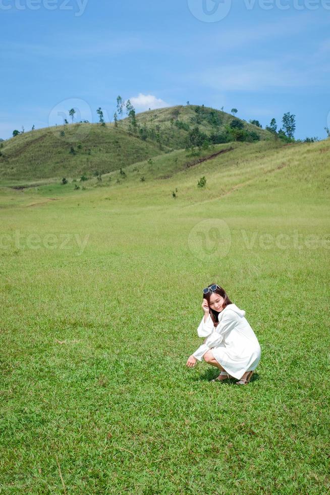 bella ragazza in piedi e recitare davanti alla montagna calva o phu khao ya con campo di erba verde e cielo blu. una delle attrazioni di viaggio naturali nella provincia di Ranong, in Thailandia foto