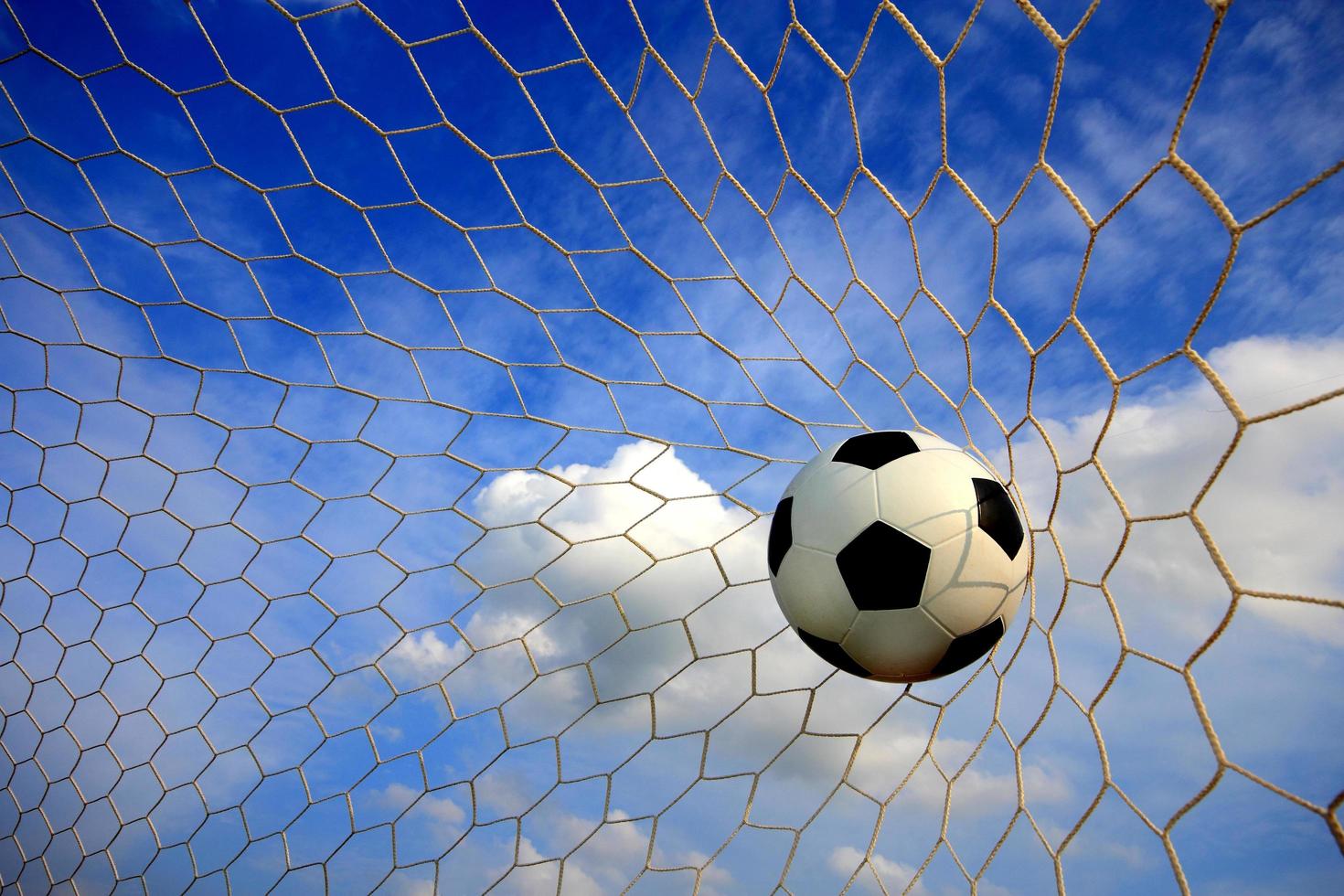 simbolo del successo e della vittoria, il pallone da calcio classico ha il colore bianco e nero che entra nella rete di porta dopo aver tirato nel gioco con uno sfondo blu cielo. concetto di successo. foto