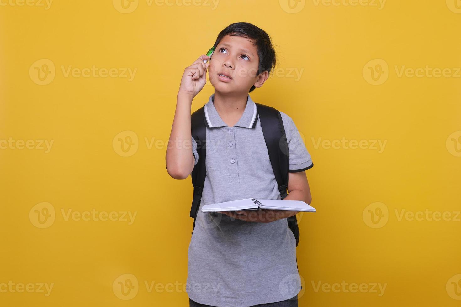 carino ragazzo asiatico in stile casual che pensa a qualcosa mentre tiene il libro, su sfondo giallo. concetto di ritorno a scuola. foto