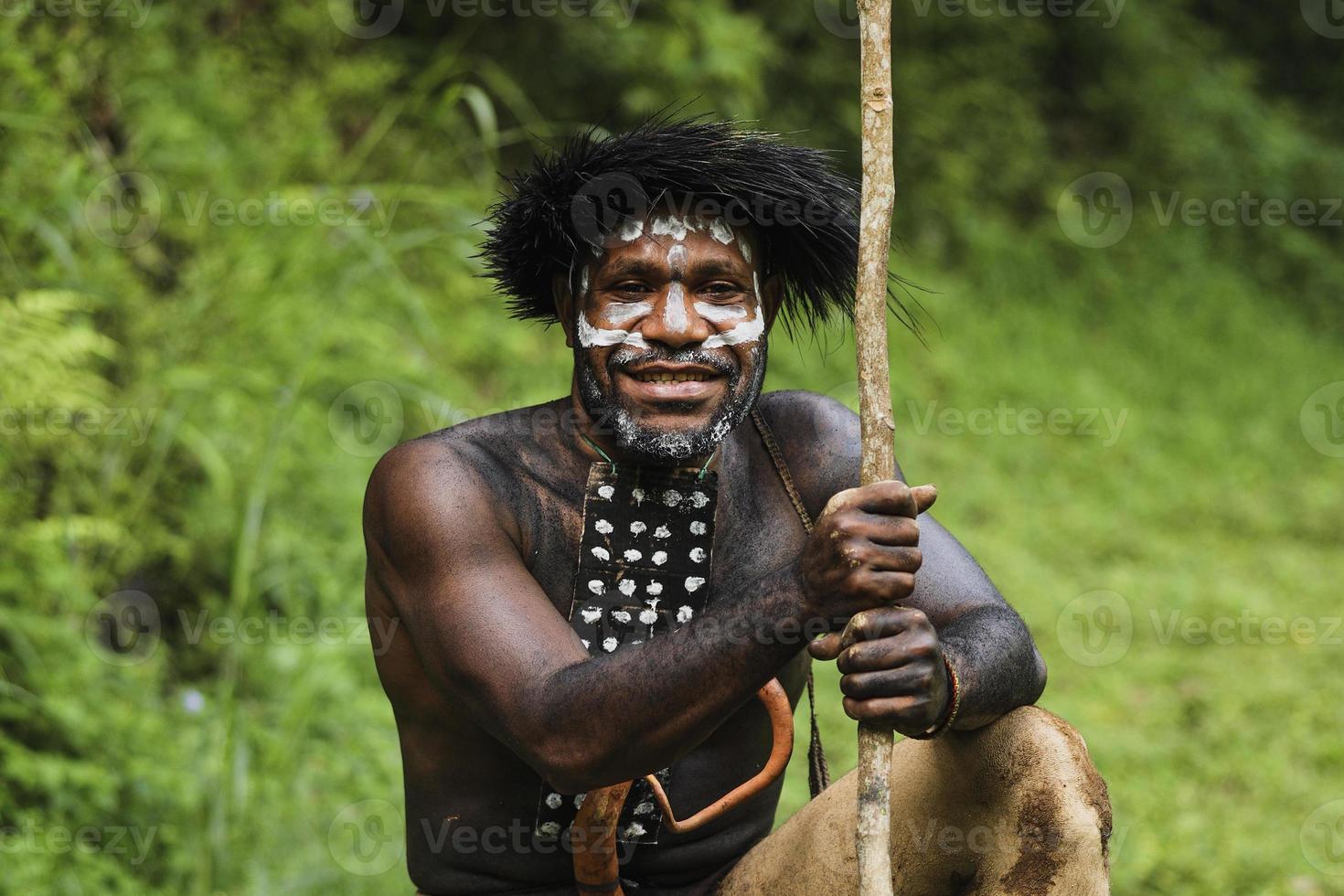 potrait di dani tribù uomo di wamena papua indonesia che indossa abiti tradizionali per la caccia sorride sullo sfondo sfocato della foresta verde. foto