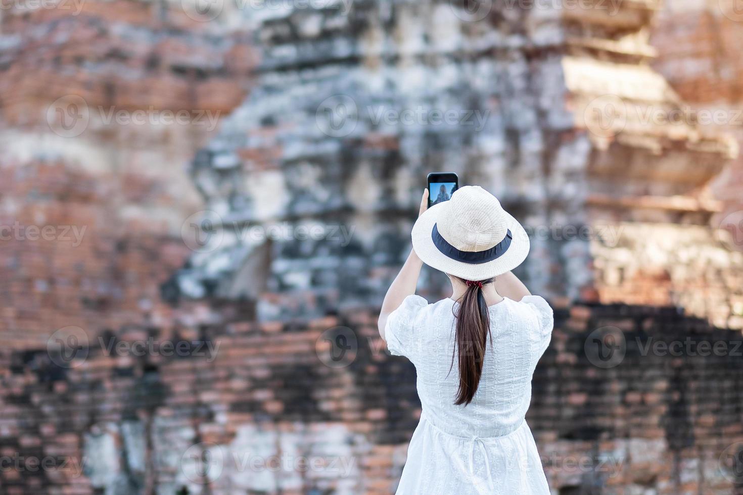 donna turistica felice in abito bianco che scatta foto con lo smartphone mobile, durante la visita al tempio di wat chaiwatthanaram nel parco storico di ayutthaya, estate, concetto di viaggio da solo, in asia e in thailandia